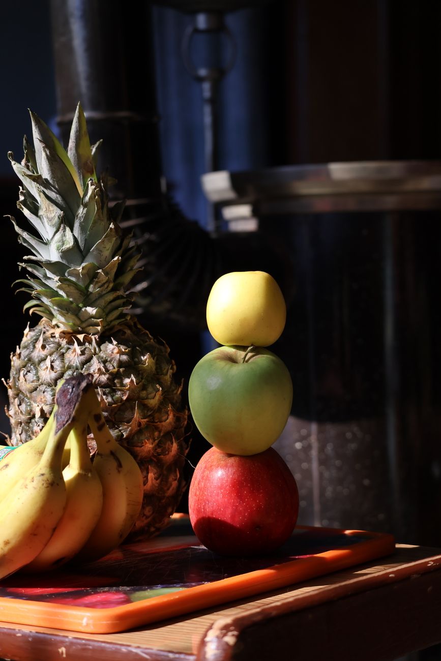 Une pile colorée de fruits dont des pommes, des bananes et un ananas sous un éclairage chaleureux.