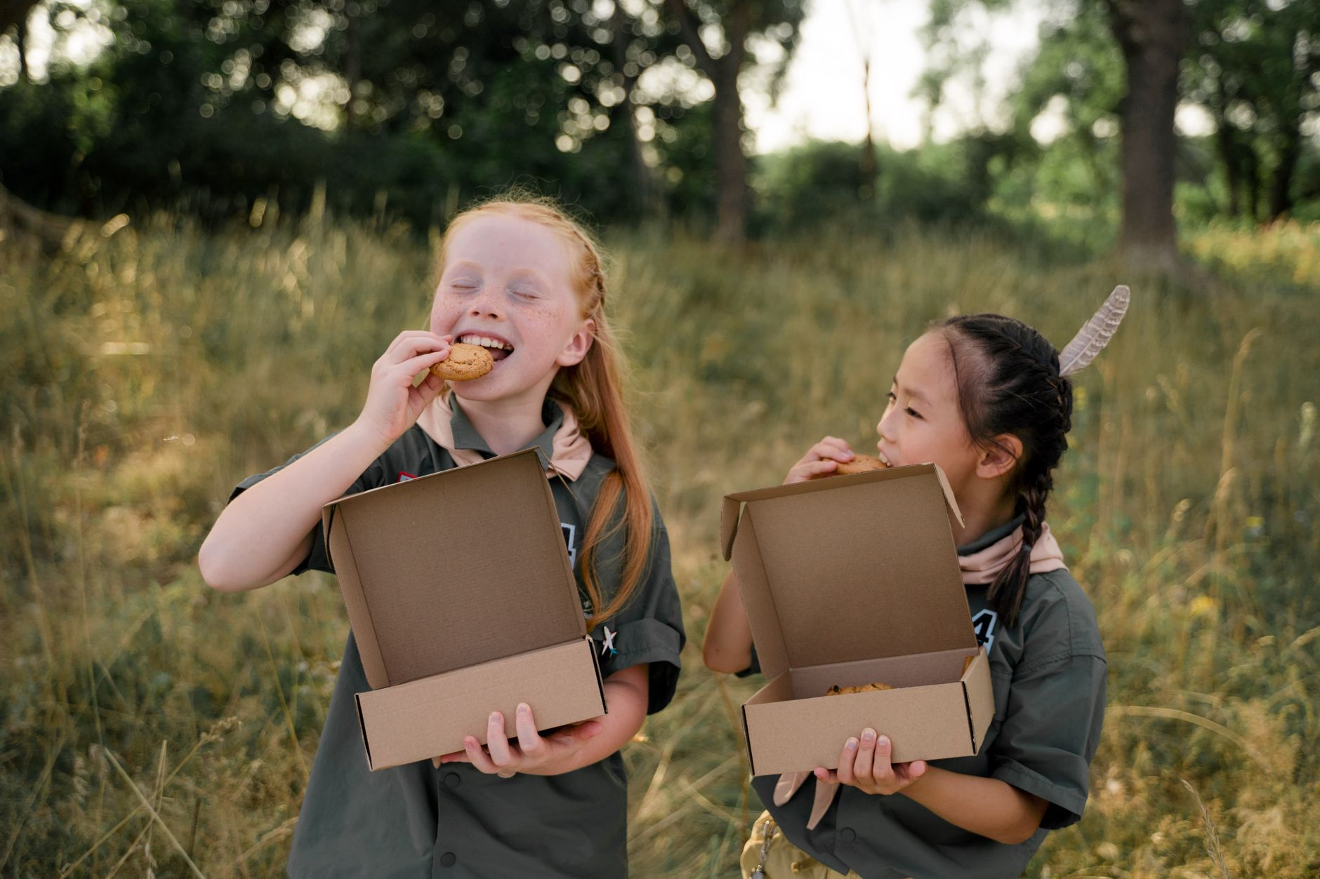Deux filles en uniforme de scout savourant des cookies dans un environnement extérieur verdoyant.
