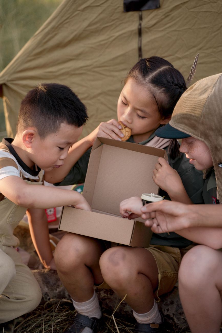 Trois enfants partageant des en-cas en plein air lors d'un camp de scouts estival.