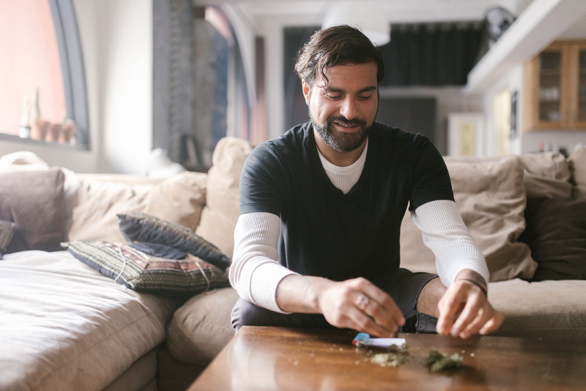 Un homme assis sur un canapé roule un joint dans un salon confortable.