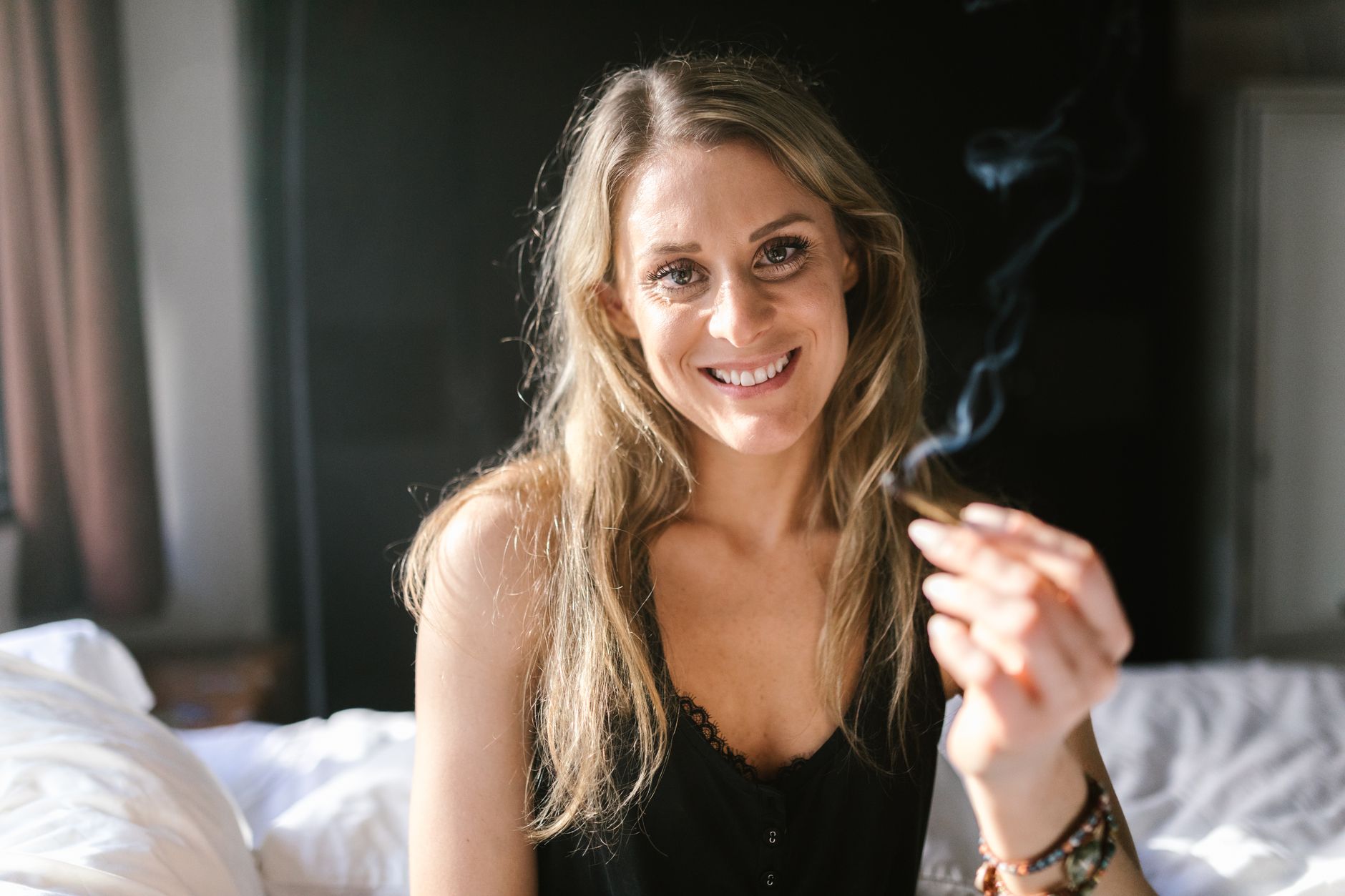 Femme souriante tenant un joint dans un cadre intérieur détendu, illustrant la culture du cannabis.
