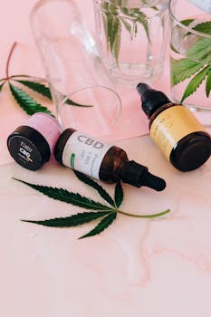 Arrangement esthétique de flacons d'huile CBD avec des feuilles de cannabis sur fond rose.