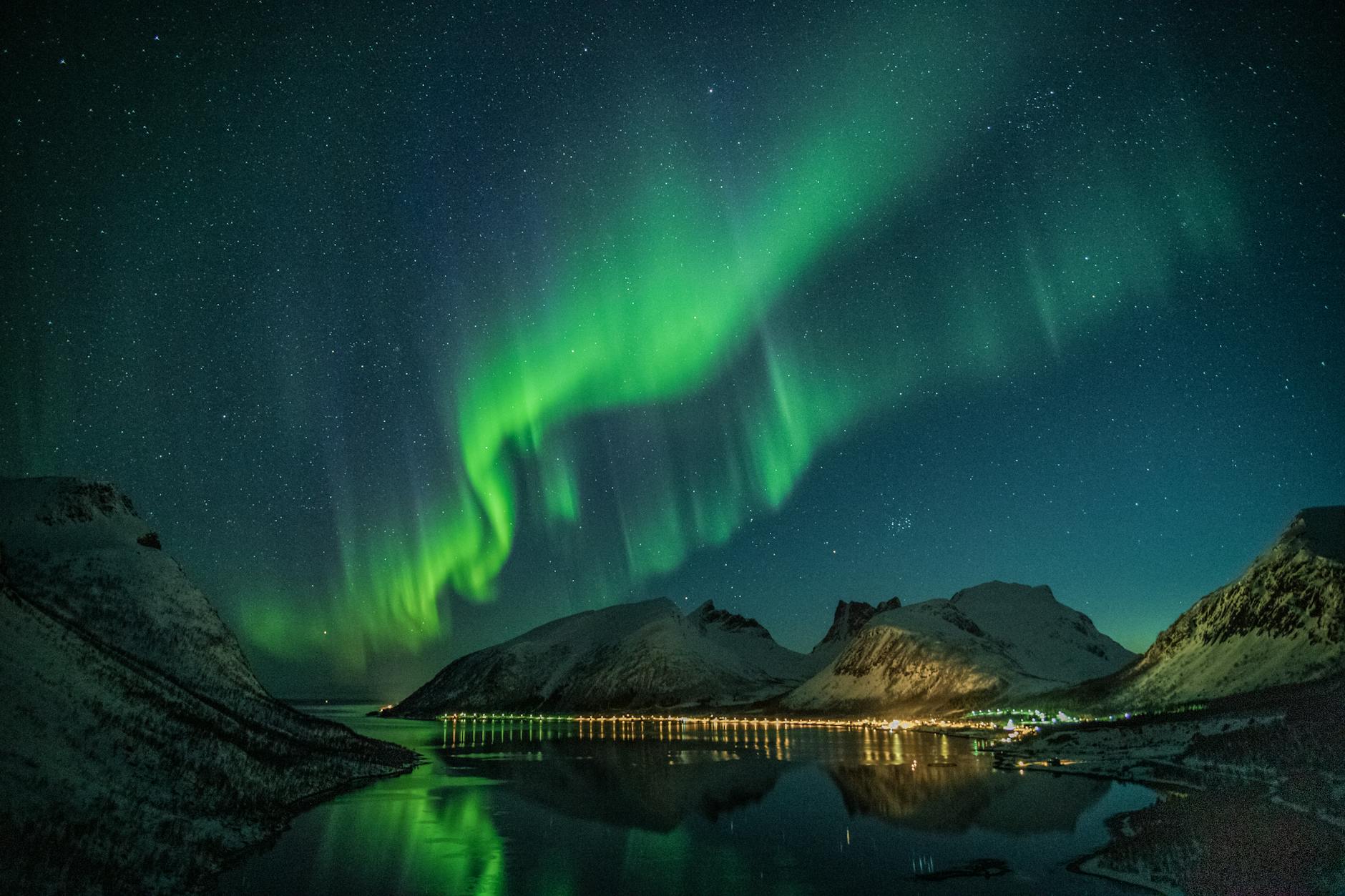 Aurores boréales envoûtantes illuminant des montagnes enneigées et se reflétant sur un lac tranquille sous un ciel étoilé.